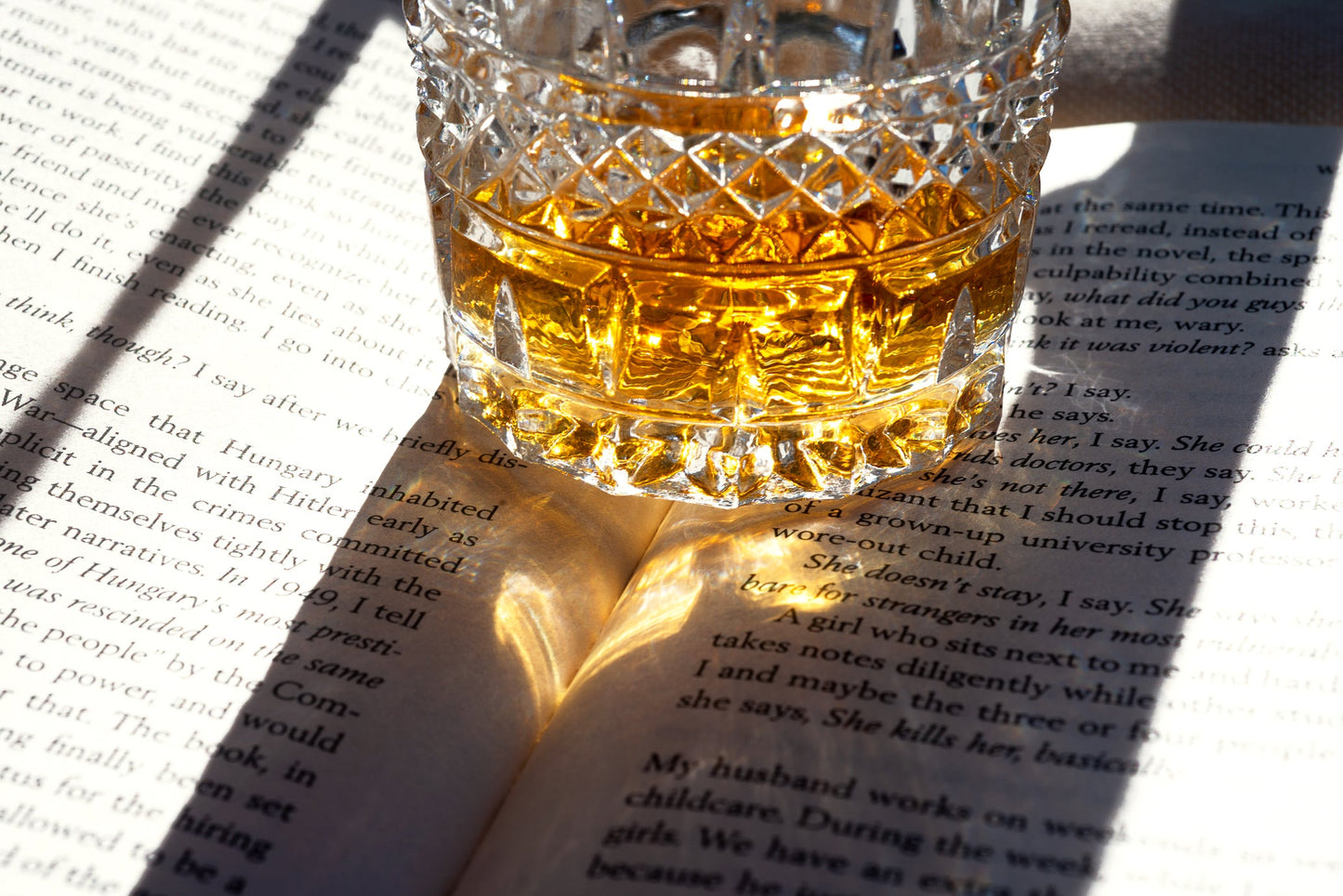Glass of whiskey on an open book with sunlight casting shadows